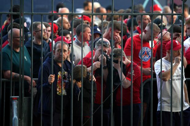 Liverpool fans cover their mouths and noses as they queue to gain entry to the Stade de France